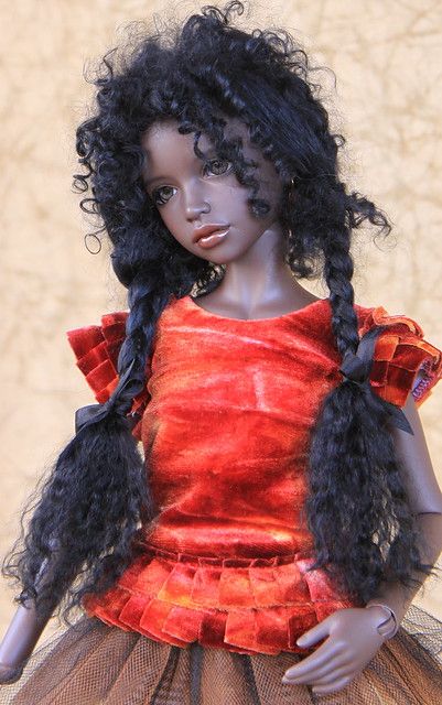 a doll with black hair wearing a red top and brown skirt, standing in front of a wall