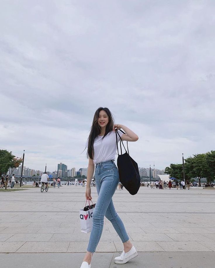 a woman is walking down the street with her hand on her hip and holding a bag