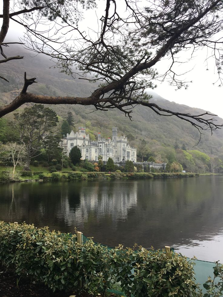 a large white house sitting on top of a lush green hillside next to a lake