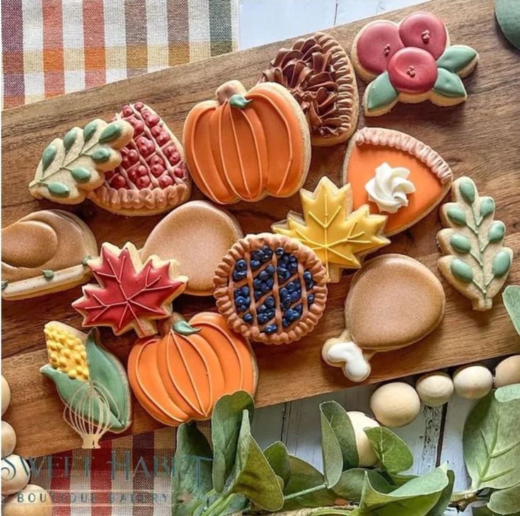 several decorated cookies sitting on top of a cutting board next to leaves and pumpkins