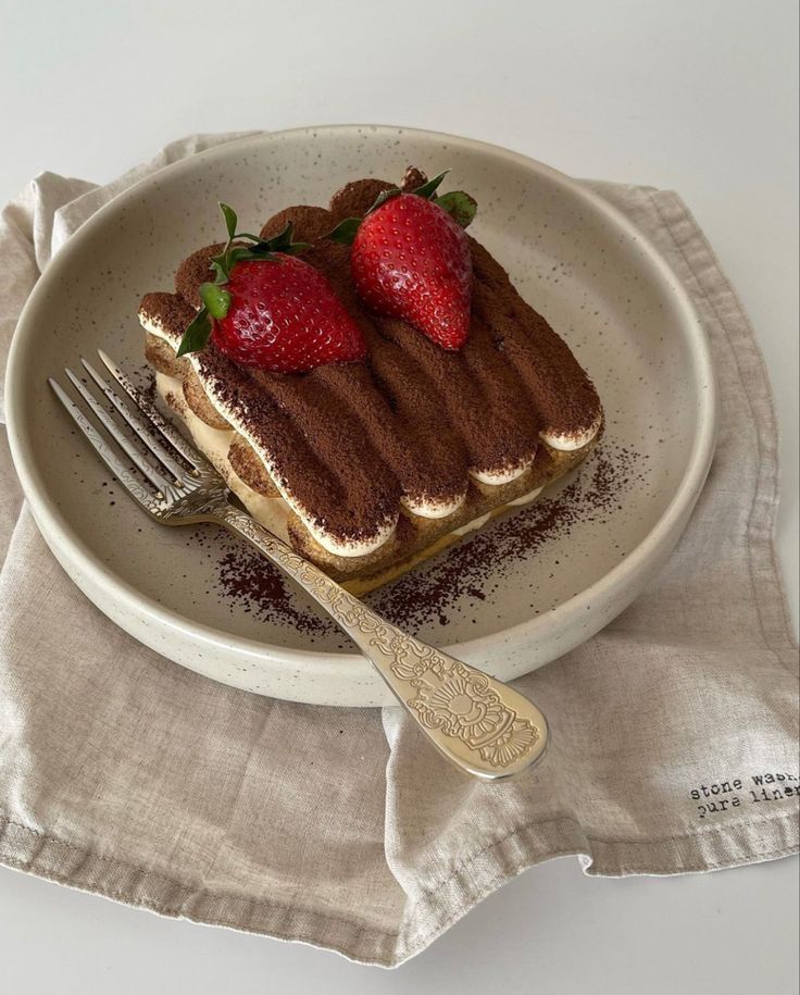 a piece of cake with strawberries on top and a fork in the bowl next to it