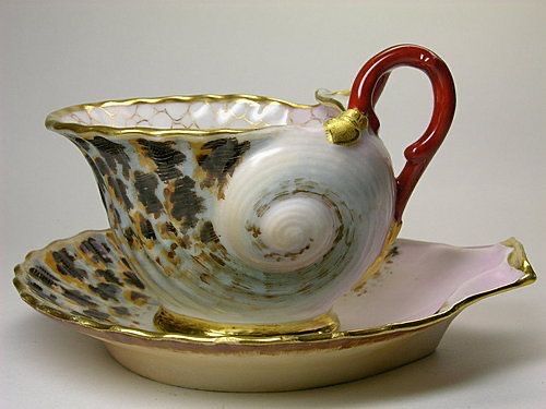 a white and gold tea cup with a red handle on the side, sitting on a saucer