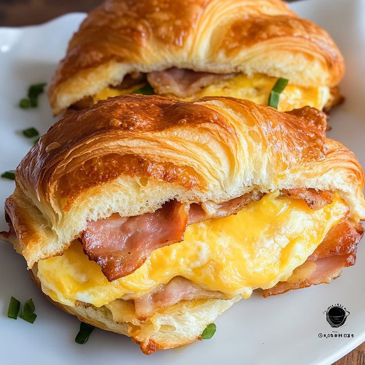 two croissants with ham and cheese are on a white plate next to each other