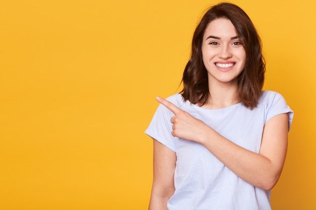 a woman pointing to the side with her finger in front of her face and wearing a white t - shirt