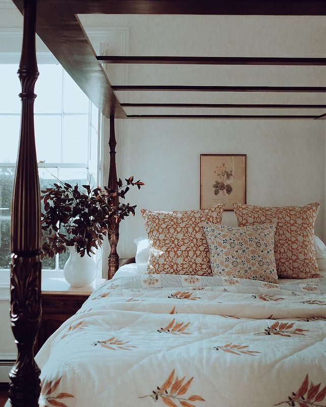 a bed with four pillows on top of it and a plant in the corner next to it