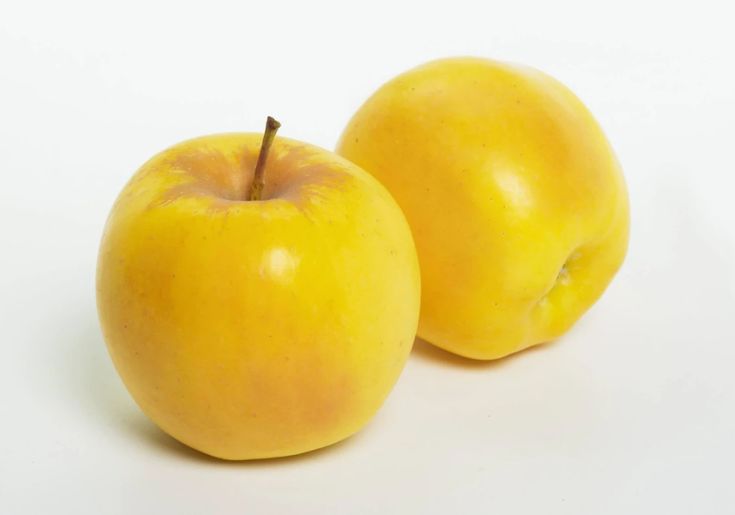 two yellow apples sitting next to each other on a white surface