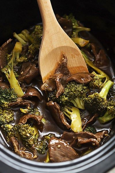 broccoli and mushrooms are being cooked in a pan with a wooden spoon on top