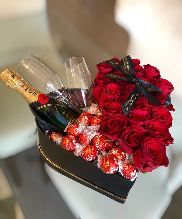 a box filled with red roses and champagne next to a bottle of wine on top of a table