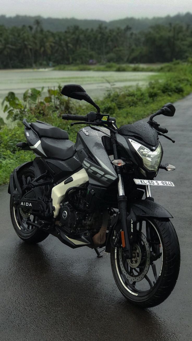 the motorcycle is parked on the side of the road by the water and trees in the background