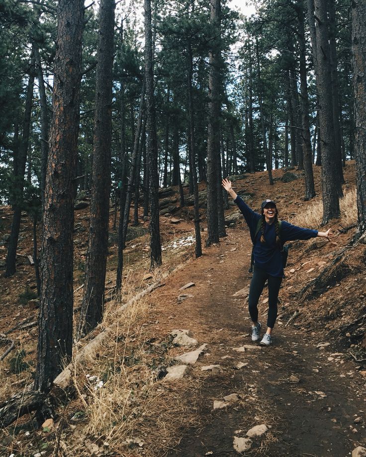 a person standing on a dirt path in the woods with their arms out and one hand up