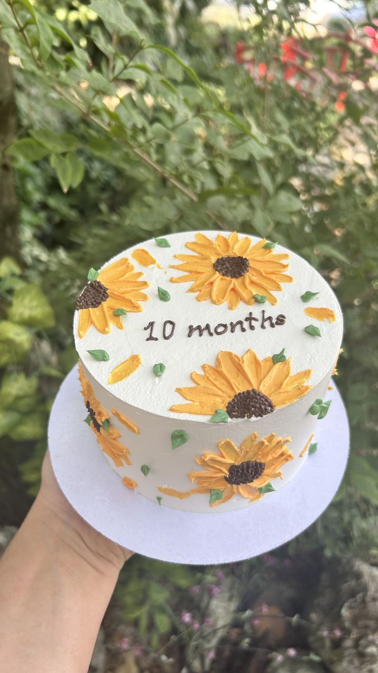 a cake with sunflowers on it is being held up by someone's hand