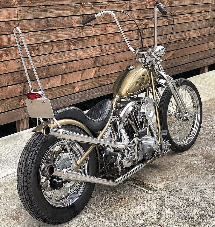 a gold motorcycle parked next to a wooden fence and building with wood slats on it