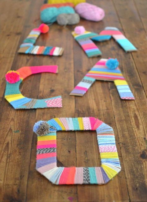 the letter e is made out of strips of yarn and paper with pom poms