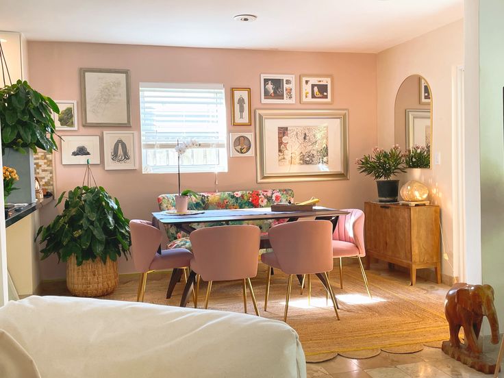 a dining room table with pink chairs and pictures on the wall in front of it