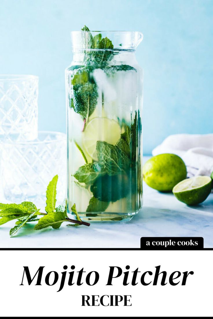 a glass jar filled with green leaves and limes next to two glasses on a table