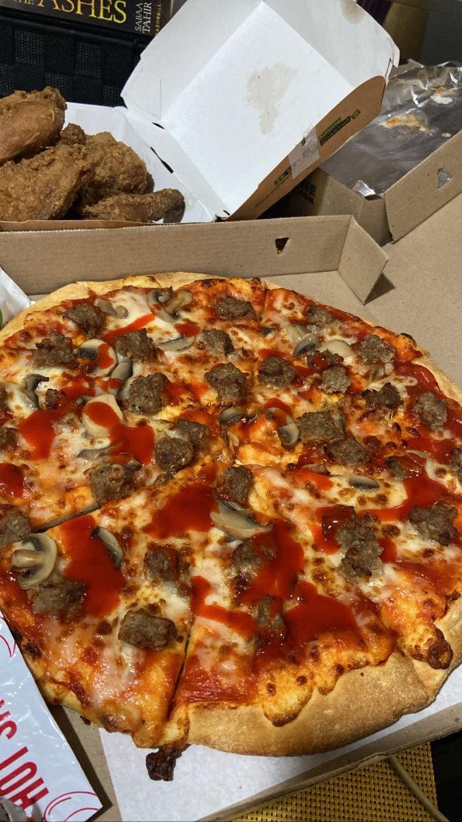 a pizza in a box with sausage, mushrooms and cheese on it next to other foods