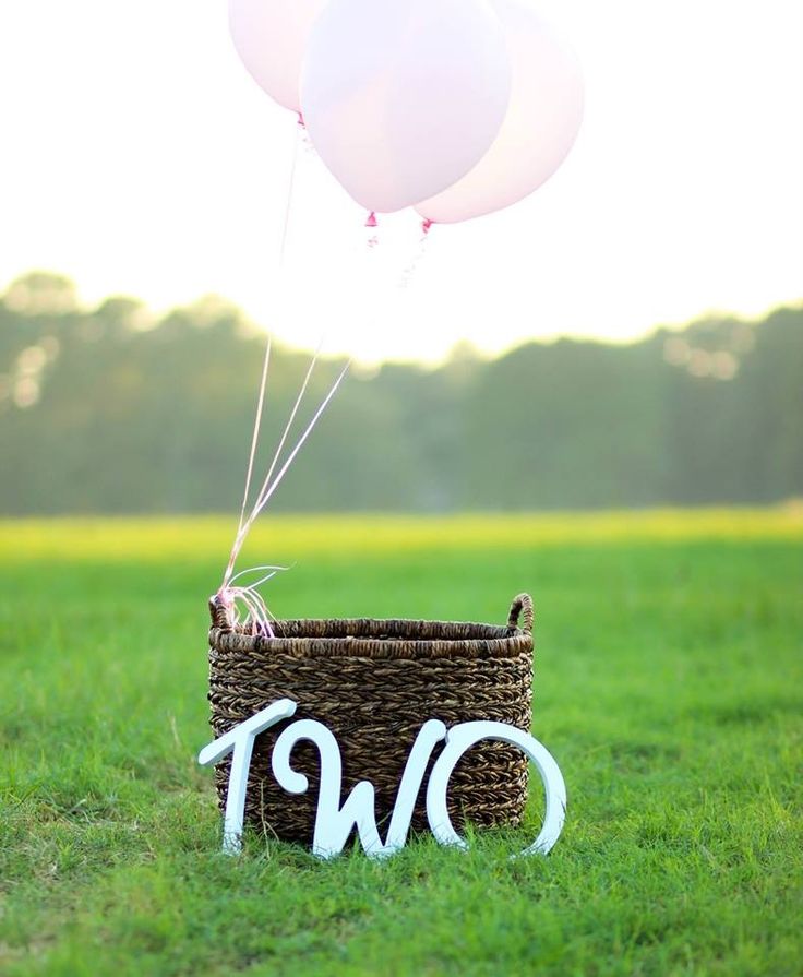 two balloons are floating in the air above a basket that says two on it and is decorated with white letters