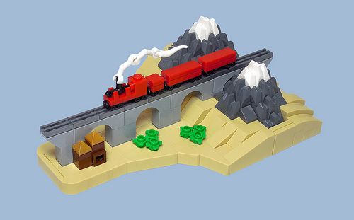 a lego train traveling over a bridge with mountains in the background