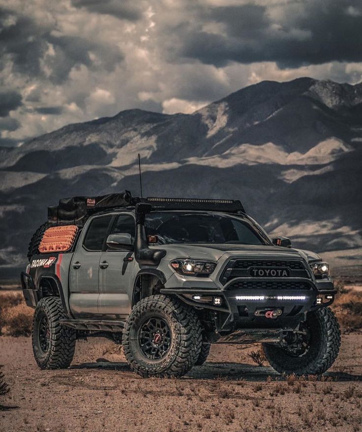 a gray truck parked on top of a dirt field next to some mountains in the background