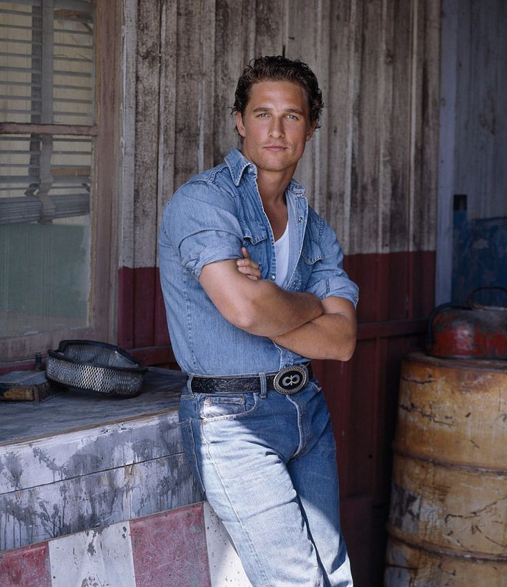 a man leaning on a wall with his arms crossed and looking at the camera while standing in front of some barrels