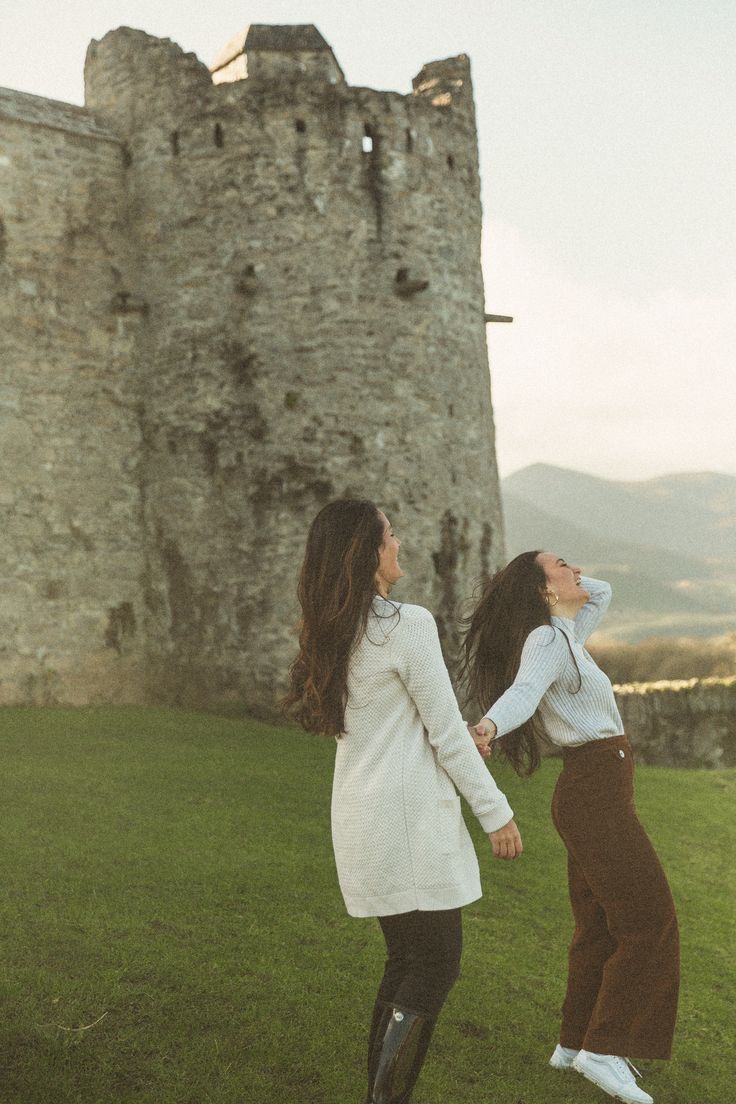 two women standing in front of a castle with one holding the other's hand