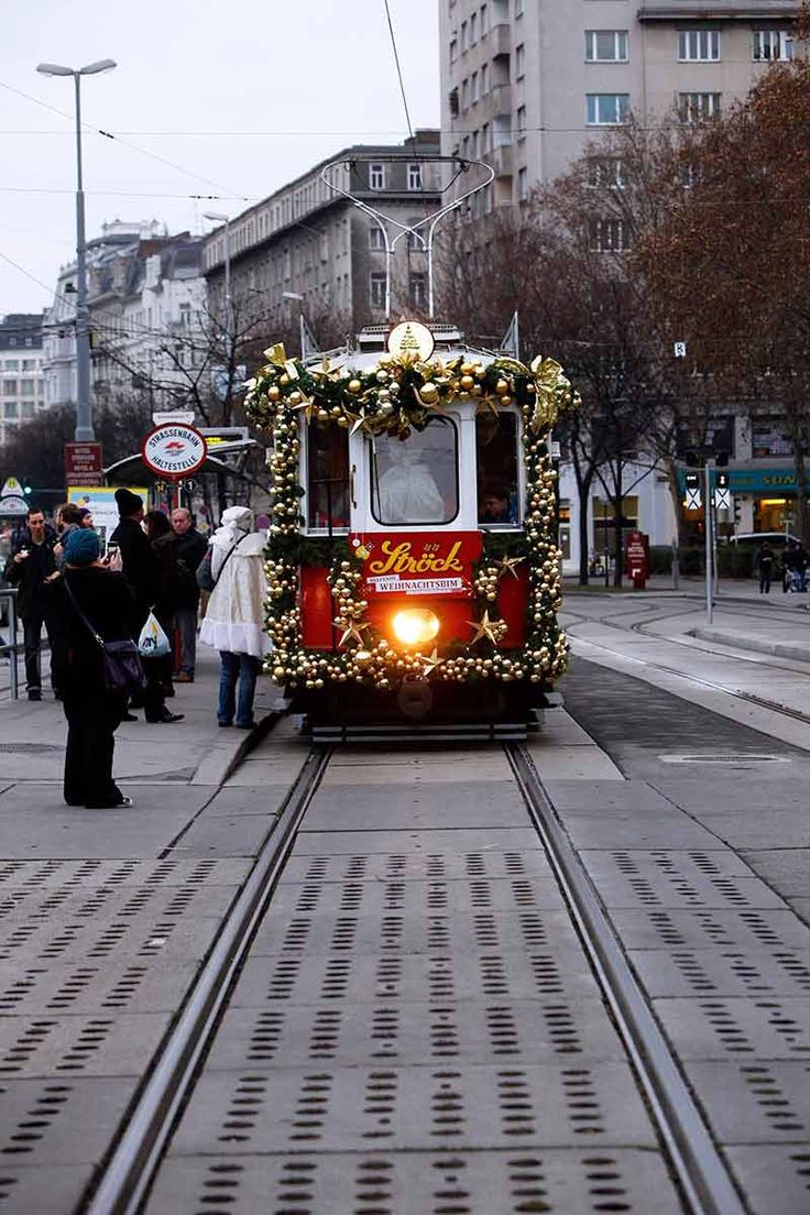 a trolley car decorated with christmas lights and garlands is coming down the tracks on a city street