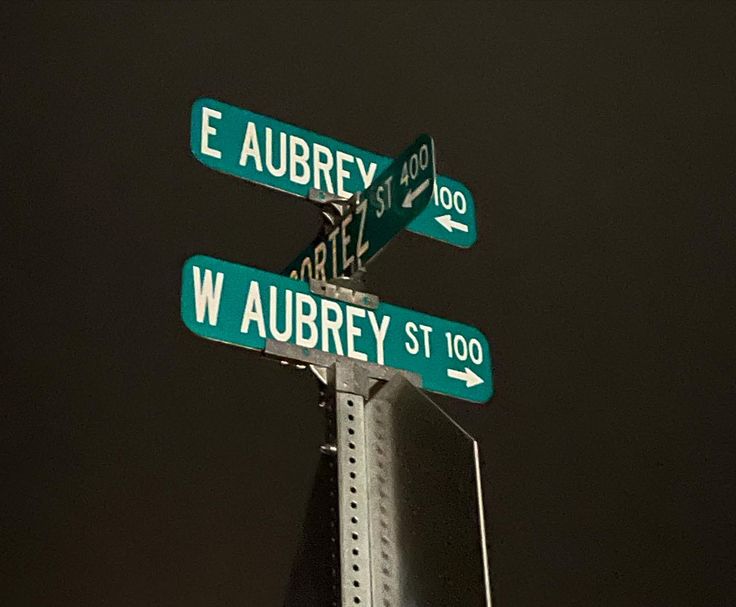 three street signs on top of a metal pole at night with the sky in the background