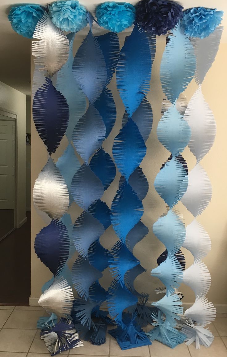 blue and white paper flowers are hanging from the ceiling in front of a wall that is decorated