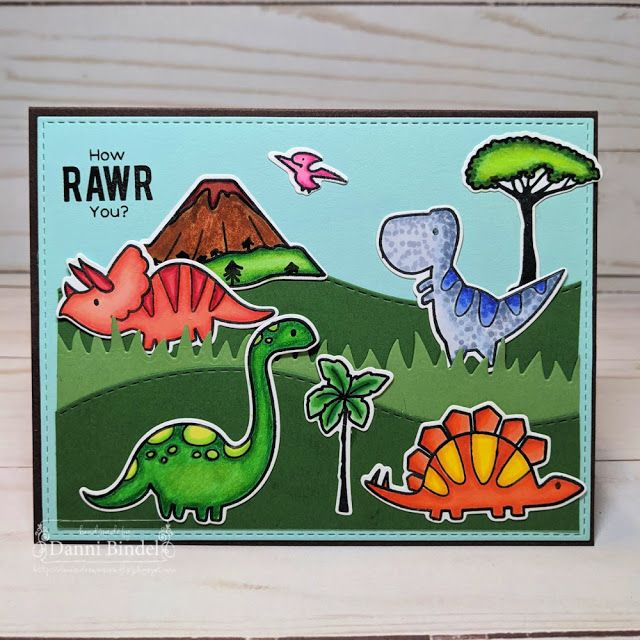 a close up of a card with dinosaurs and trees in the background, on a wooden surface