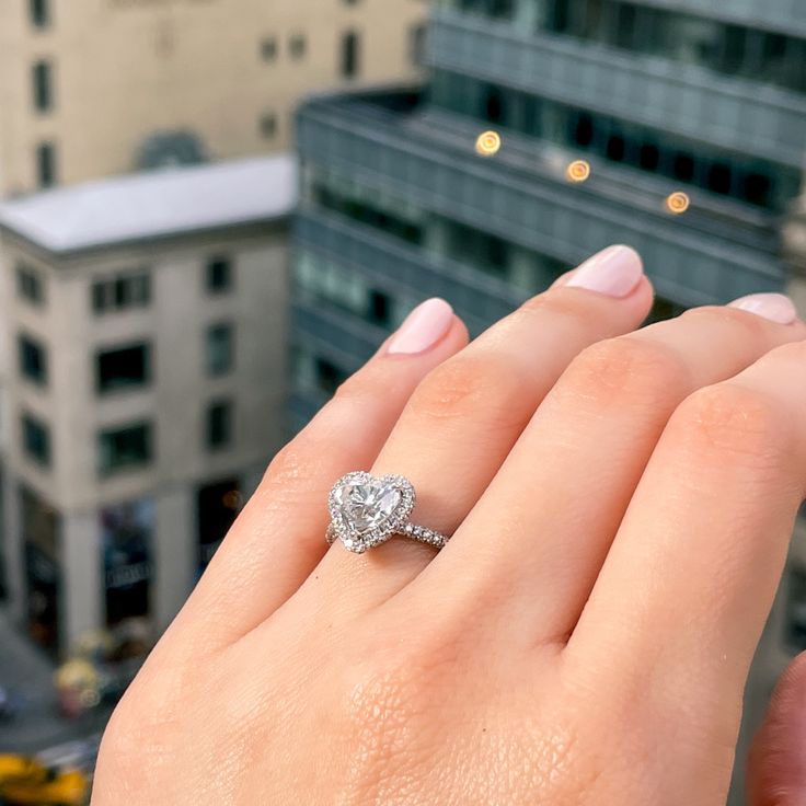 a woman's hand with a diamond ring on top of her finger and buildings in the background