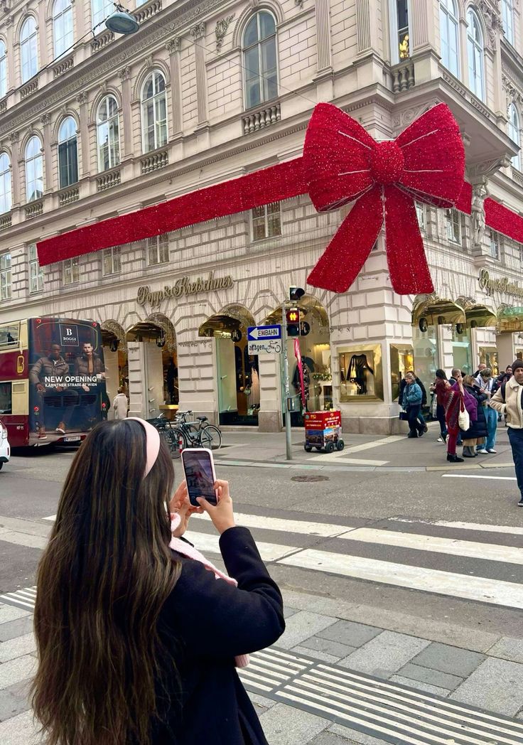 a woman taking a photo of a large red bow on the side of a building