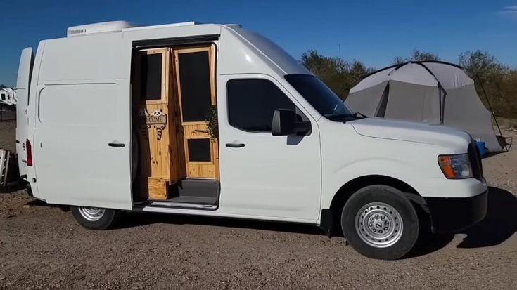 a white van is parked in the dirt with its door open and it's tent opened