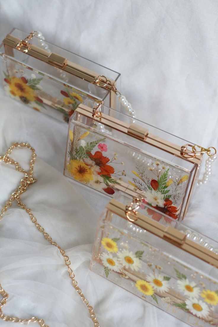 three clear purses sitting on top of a white bed next to a gold chain