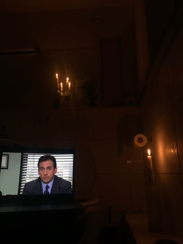 a man in a dark room on a television screen with candles lit up behind him