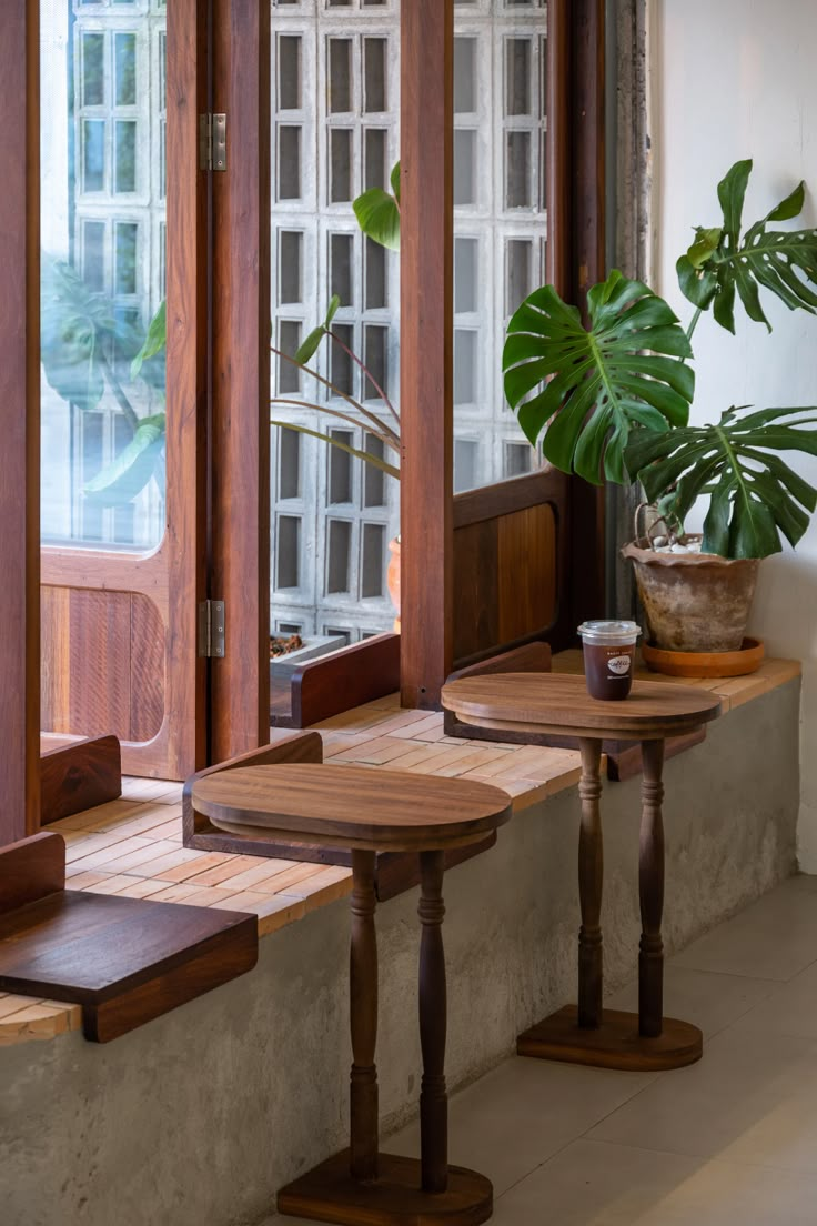 two wooden tables sitting next to each other near a window with potted plants on it