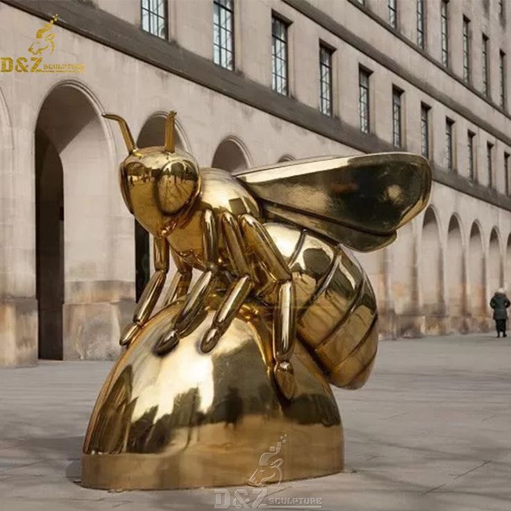 a golden bee statue sitting on top of a metal object in front of a building