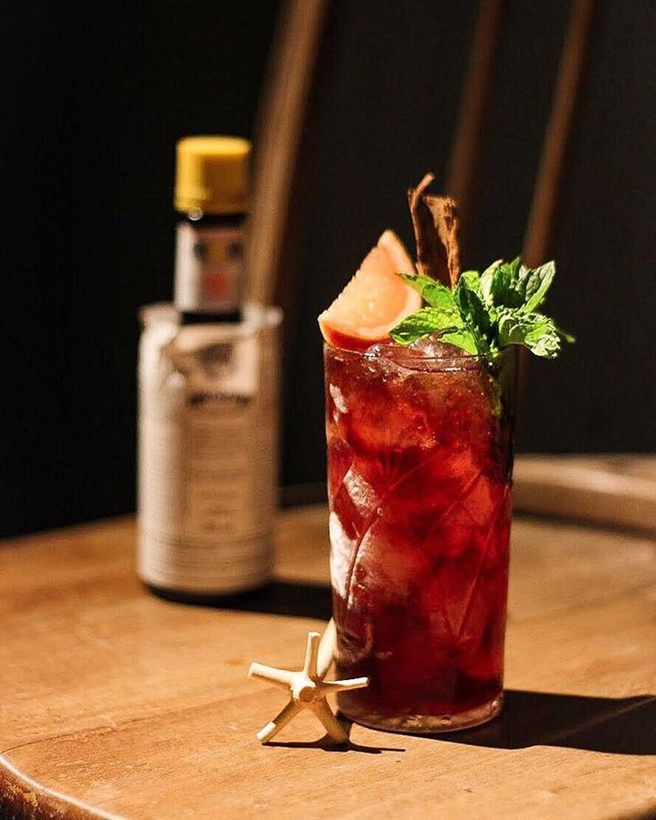 a tall glass filled with red liquid and garnish on top of a wooden table