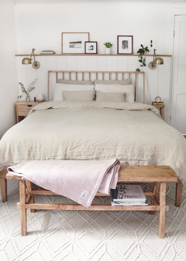 a bed with white linens and pillows in a small room next to a wooden bench