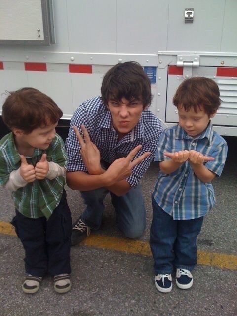 two young boys standing next to a man giving the peace sign with their hands in front of them