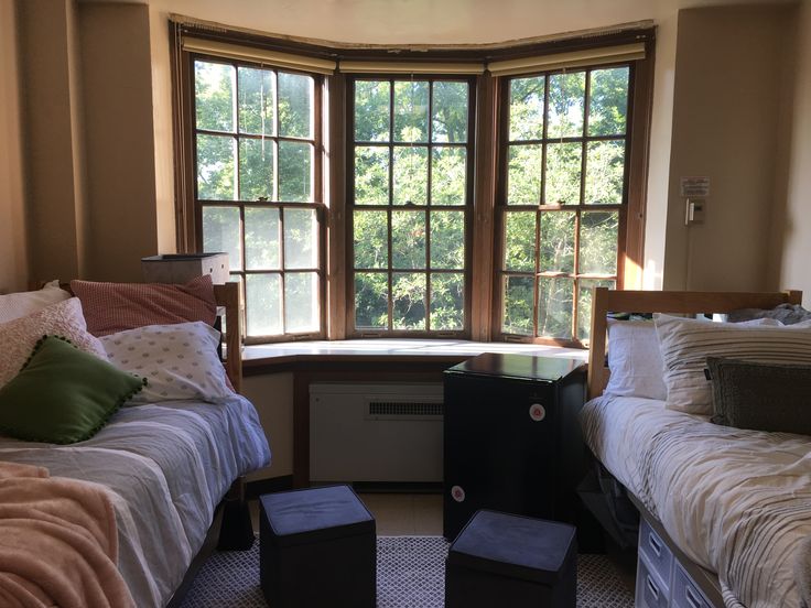 there are two beds in the room with pillows on them and one is next to a window