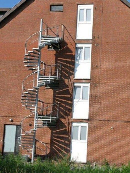 a tall brick building with a metal spiral staircase next to the door and windows on each side