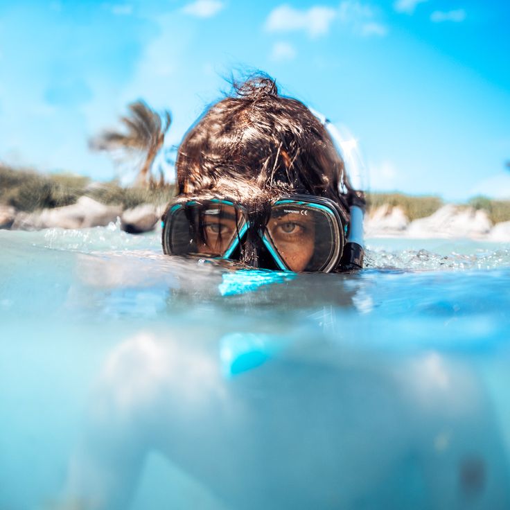 a woman wearing goggles and snorkels swimming in the ocean with her head under water