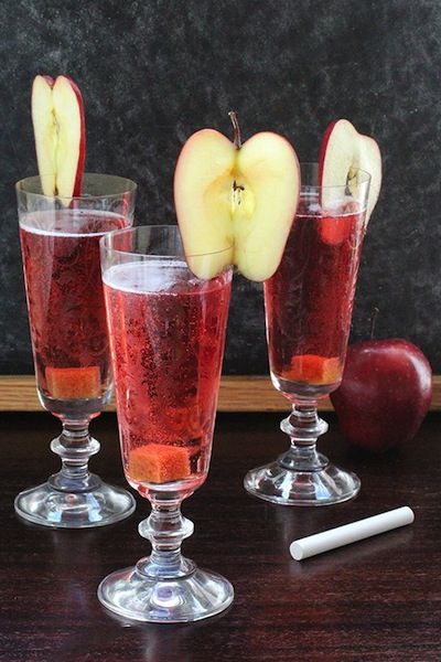 three wine glasses filled with red liquid and apple slices next to an chalkboard background