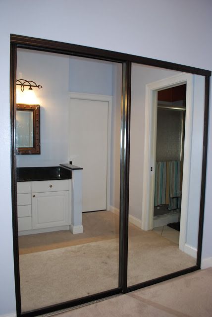 an empty bathroom is reflected in the mirrored door of another room that has a sink and mirror on it