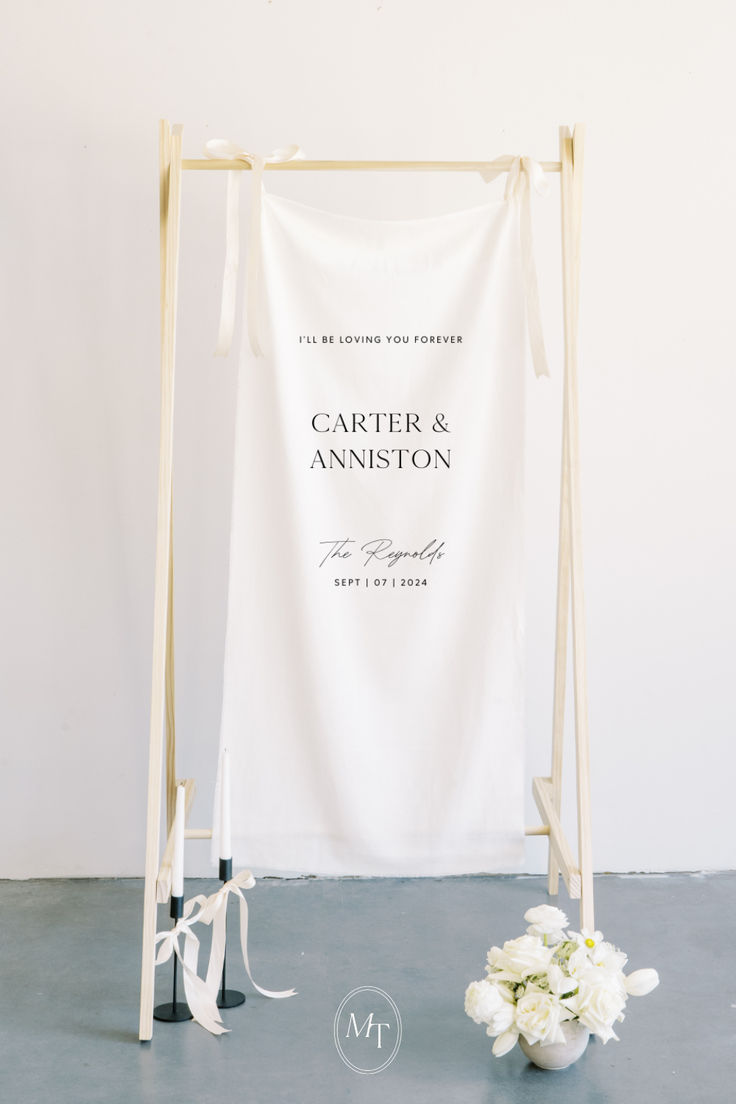 a white wedding sign with flowers on the floor next to it and a vase full of flowers