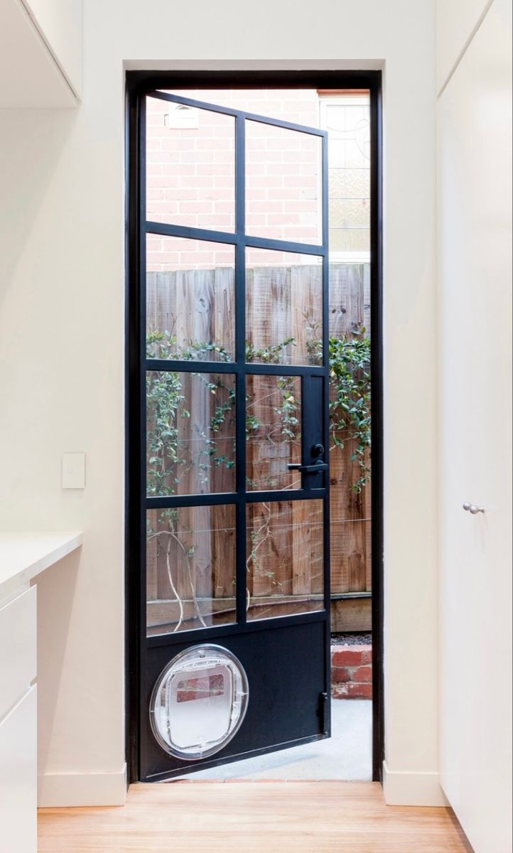 an open door leading to a patio with a fence in the back ground and potted plants on either side