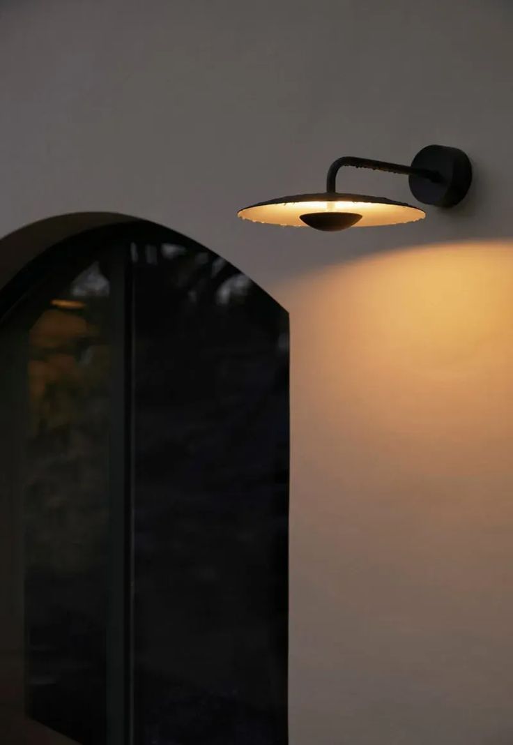 a wall light that is on the side of a building with an arched window behind it