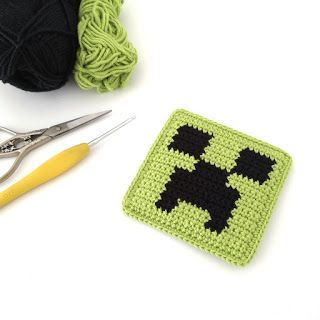 a crocheted square next to a pair of scissors, yarn and knitting needles