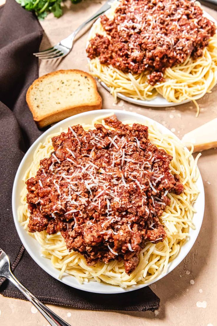 two plates of spaghetti with meat sauce and bread