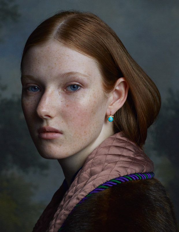 a woman with freckled hair and blue eyes is posing for a portrait in front of a dark background